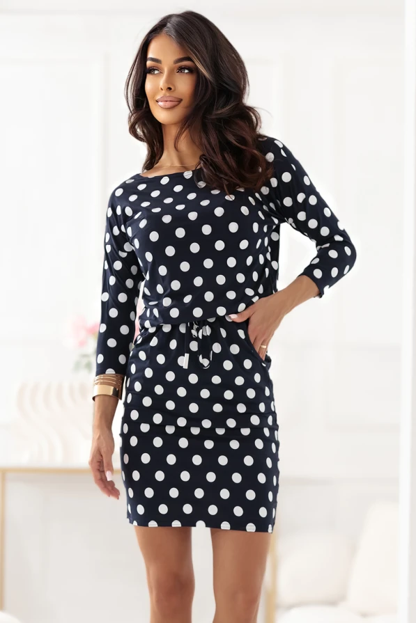 Modelka prezentuje granatową sukienkę z białymi grochami marki Numoco. Sukienka z długim rękawem, kieszeniami i wiązaniem w pasie. Styl casual, idealna na co dzień. Produkcja polska.