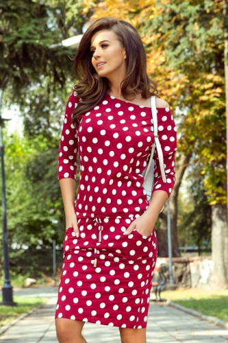 A woman is wearing a stylish, knee-length, red dress with white polka dots, featuring three-quarter sleeves and a drawstring waist. The dress has a casual yet chic look, perfect for a day out.}