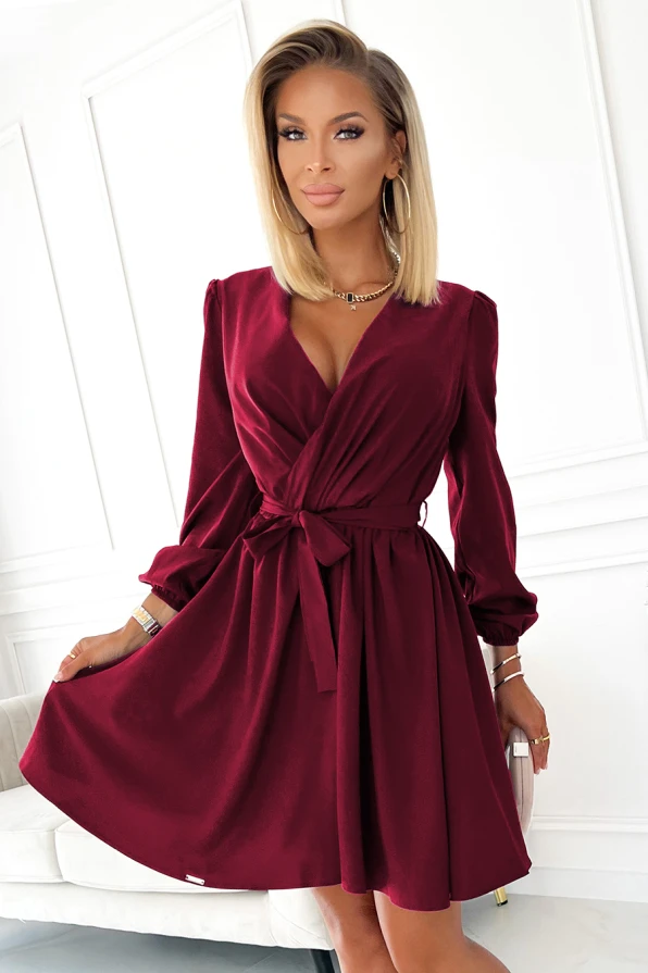 A woman is wearing an elegant, deep red dress with a wrap-style front and a tied waist, creating a flattering silhouette. The dress features long sleeves with subtle puff details, adding a touch of sophistication.