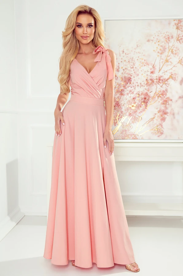 A long, elegant pink dress with a fitted bodice and a flowing skirt, featuring a stylish bow on one shoulder. The dress exudes sophistication, perfect for formal occasions or evening events.