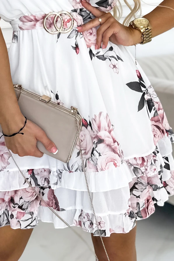 A floral dress with a layered ruffle skirt features a delicate pink and white pattern, complemented by a stylish belt with a double-ring buckle. The outfit is accessorized with a beige clutch and a gold watch, adding a touch of elegance.