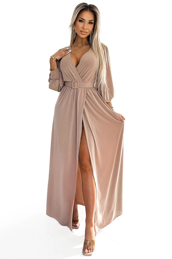A long, elegant dress in a soft beige color features a deep V-neckline and a stylish belt at the waist. The flowing fabric and high slit add a touch of sophistication and allure.