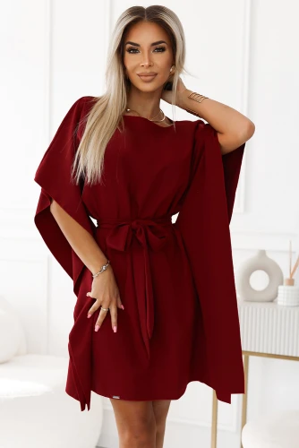 A woman is wearing an elegant burgundy dress with a flowing cape design and a matching waist tie. The dress features a simple round neckline and is styled in a modern, sophisticated manner.}