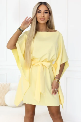 The model presents the Numoco pastel lemon mini dress featuring loose kimono-style sleeves and a waist tie that beautifully defines the figure. An elegant, lightweight piece, perfect for summer, parties and stylish outings.}