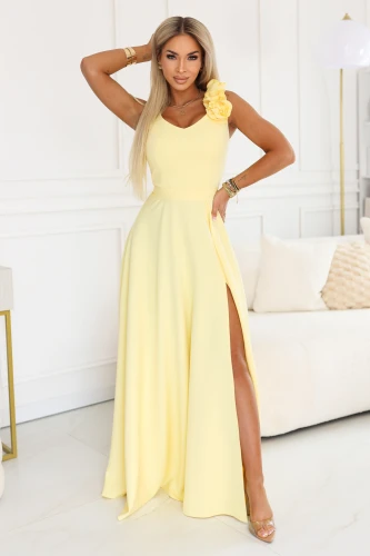Elegant yellow Numoco Poland maxi dress with a floral detail on the shoulder, V-neckline, high slit, accentuated waist and a flowing skirt, perfect for a wedding, prom, ball and summer celebrations.}