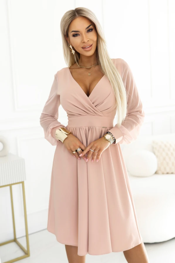 The model presents an elegant beige midi dress with a wrap neckline, flared skirt and light transparent sleeves. The dress is ideal for a wedding, communion, christening and family celebrations, beautifully accentuating the waist and feminine figure.