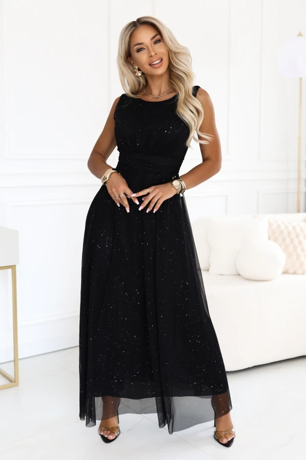 Model wearing a black, shimmering maxi dress Numoco Basic with an accentuated waist and flared hem.
