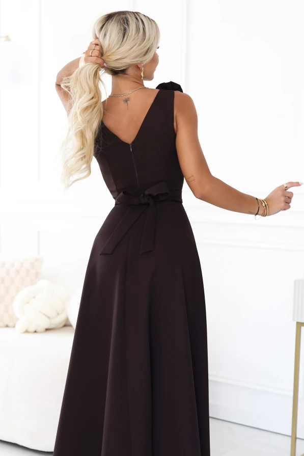 Model wearing an elegant chocolate brown maxi dress with a sweetheart neckline, leg slit and a decorative flower on the shoulder.