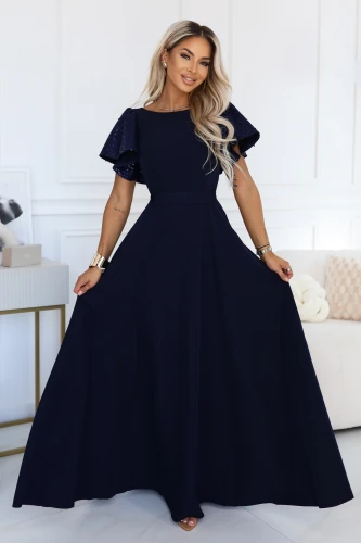 Model wearing a navy blue Numoco maxi dress with a fitted waist, flared skirt and shimmering butterfly-style sleeves.}