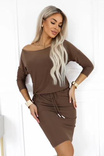 Model wearing a sporty Numoco dress in mocha brown, with a boat neckline baring one shoulder, 3/4 sleeves, pockets and a waist tie.}