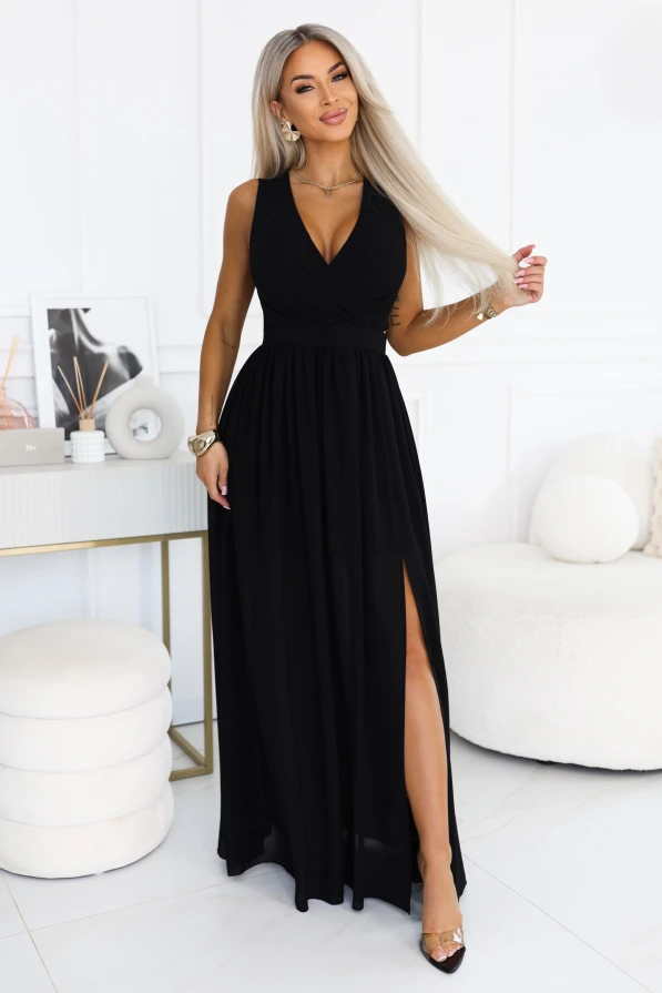 Model wearing the black chiffon JUSTINE maxi dress by Numoco, with a wrap neckline, wide straps, an accentuated waist and an airy bottom with a high leg slit.