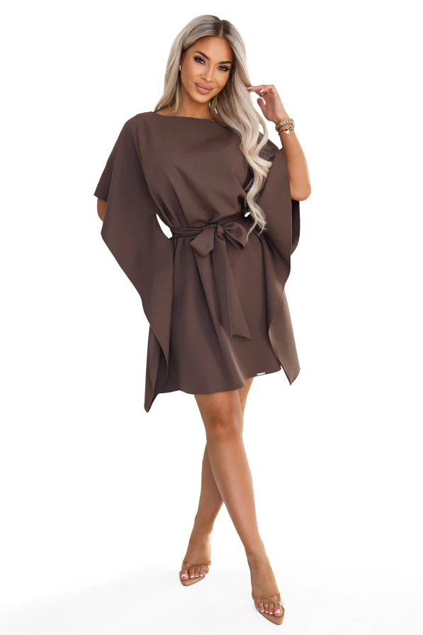 Model wearing the SOFIA dress by Numoco in a mocha brown shade. The dress reaches just above the knee, with a boat neckline, wide butterfly sleeves and a belt tied at the waist in a bow.
