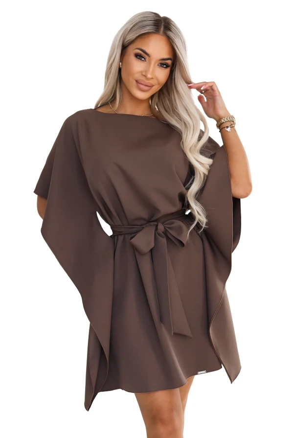 Model wearing the SOFIA dress by Numoco in a mocha brown shade. The dress reaches just above the knee, with a boat neckline, wide butterfly sleeves and a belt tied at the waist in a bow.