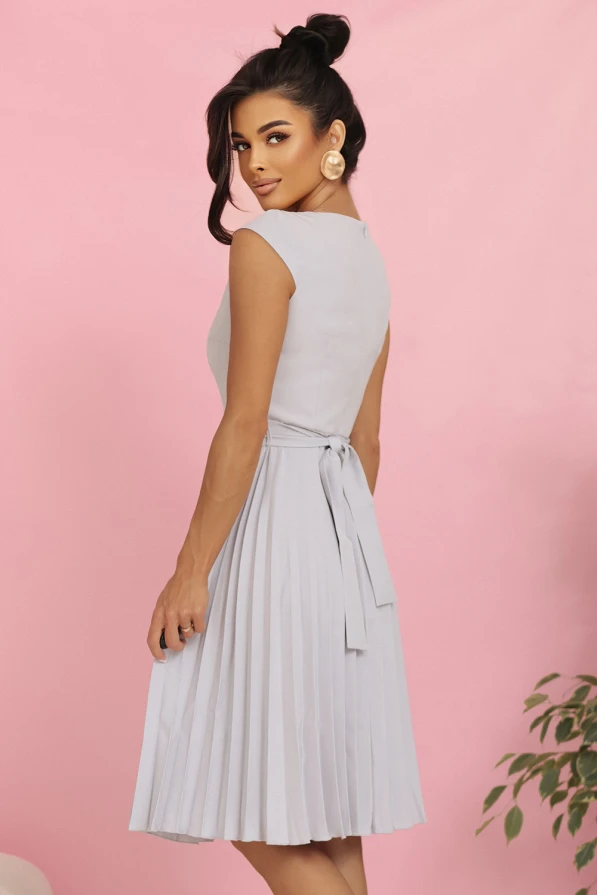 Modelka w eleganckiej plisowanej sukience midi marki Numoco w kolorze jasnoszarym, z krótkim rękawkiem i wiązaniem w talii, prezentująca kreację idealną na wesele, komunię i inne uroczystości.