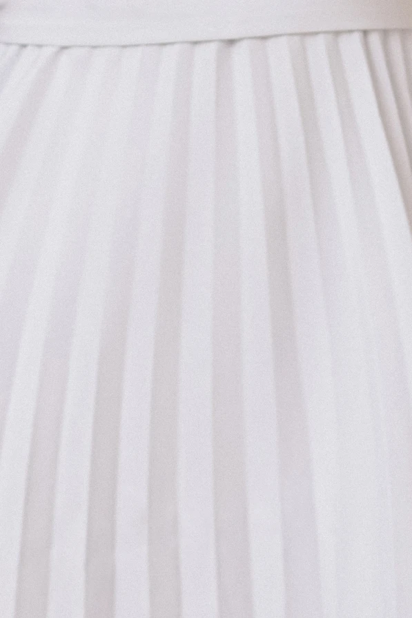 Modelka w eleganckiej plisowanej sukience midi marki Numoco w kolorze jasnoszarym, z krótkim rękawkiem i wiązaniem w talii, prezentująca kreację idealną na wesele, komunię i inne uroczystości.