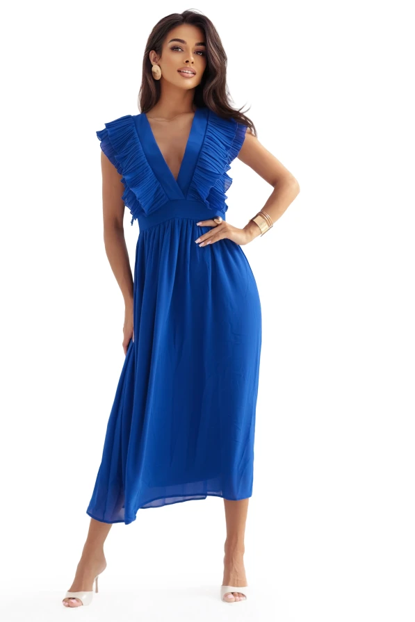 Kobieta w eleganckiej, chabrowej sukni midi z falbanami przy dekolcie i rozkloszowanym dołem, pozująca w jasnym, stylowym wnętrzu. Limitowana edycja sukienki marki Numoco, produkt polski.