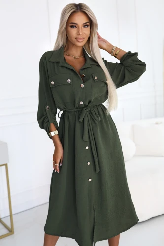 Stylowa sukienka koszulowa w kolorze khaki, z wiązaniem w pasie, guzikiem zapinana na całej długości, długi rękaw z podpięciem, elegancki fason marki Numoco Basic, europejska produkcja, prezentacja na modelce w nowoczesnym wnętrzu.}