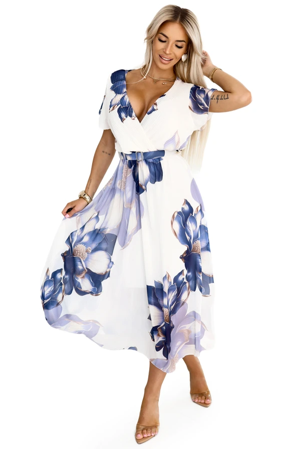 Modelka z uśmiechem prezentuje lekką, szyfonową sukienkę midi z kwiatowym wzorem w odcieniach niebieskiego. Stylizacja emanuje kobiecą delikatnością i letnim wdziękiem, idealna na wyjątkowe okazje i codzienne chwile.