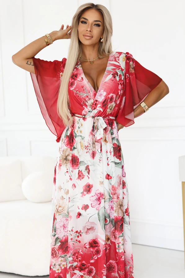 Zwiewna maxi sukienka Numoco z kopertowym dekoltem i szerokimi rękawkami, w kwiecisty wzór z czerwonymi różami, uszyta z lekkiego szyfonu. Modelka prezentuje elegancki, romantyczny fason, który pięknie podkreśla sylwetkę i dodaje kobiecego uroku.