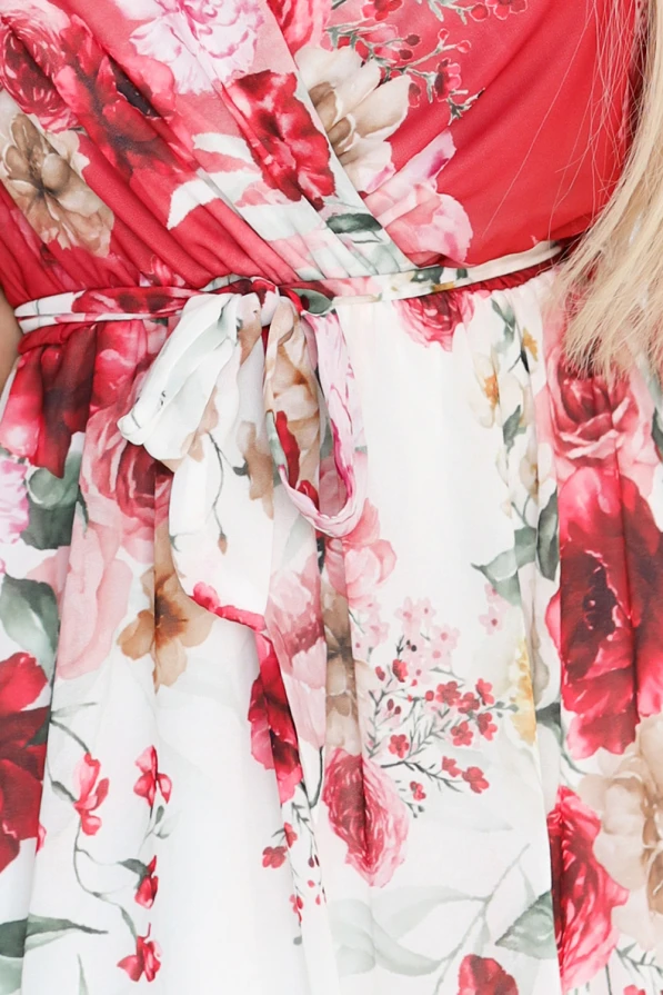 Zwiewna maxi sukienka Numoco z kopertowym dekoltem i szerokimi rękawkami, w kwiecisty wzór z czerwonymi różami, uszyta z lekkiego szyfonu. Modelka prezentuje elegancki, romantyczny fason, który pięknie podkreśla sylwetkę i dodaje kobiecego uroku.