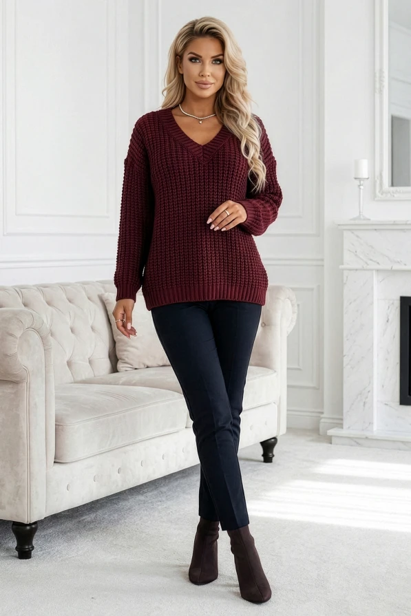 Kobieta w bordowym swetrze oversize, dekolt V, w białym wnętrzu. Stylowa moda